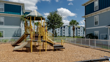 Playground at The Enclave at Tranquility Lake in Riverview, FL, with colorful play equipment, safety flooring, and surrounded by lush greenery.