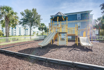 Playground at The Enclave at Tranquility Lake in Riverview, FL, with colorful play equipment, safety flooring, and surrounded by lush greenery.