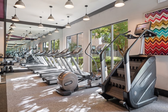 A well-equipped fitness center, featuring expansive windows, a variety of cardio and weight equipment, and mirrors to enhance your workout experience.