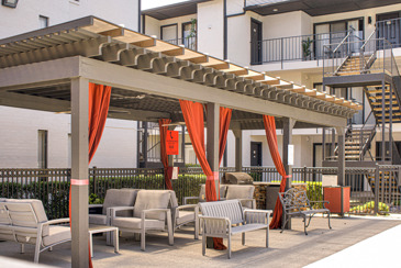 The covered pool pergolas at the pool area with orange curtains and lounge chairs at Vue at Knoll Trail in Dallas, TX. 