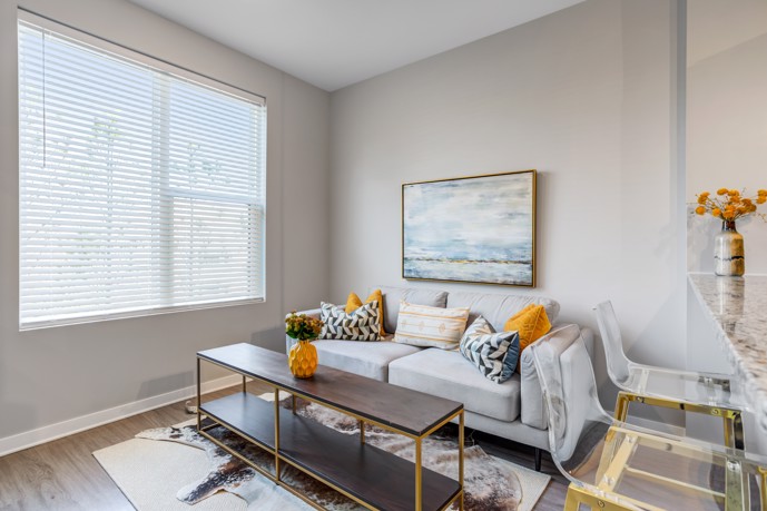 A cozy living room within Views of Music City, featuring a comfortable couch, abundant natural light pouring in through large windows, and kitchen bar stools conveniently placed nearby for dining or socializing.