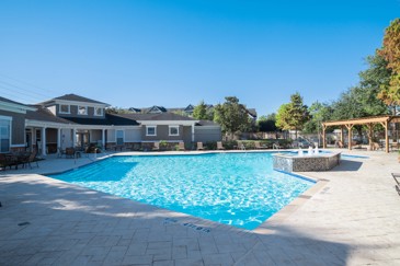 Large grey paved patio and swimming pool with apartment building behind it