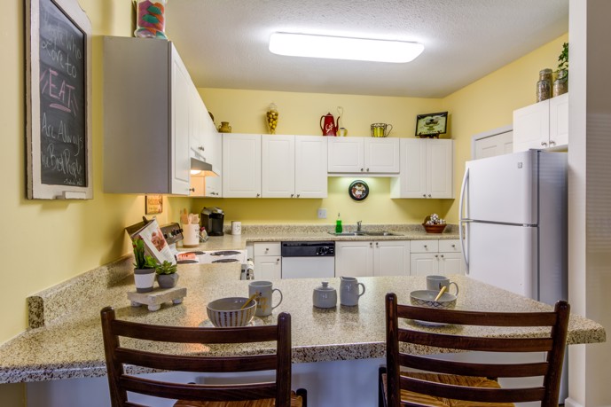 A kitchen at Sugar Mill apartments with a white refrigerator, microwave, and two chairs.