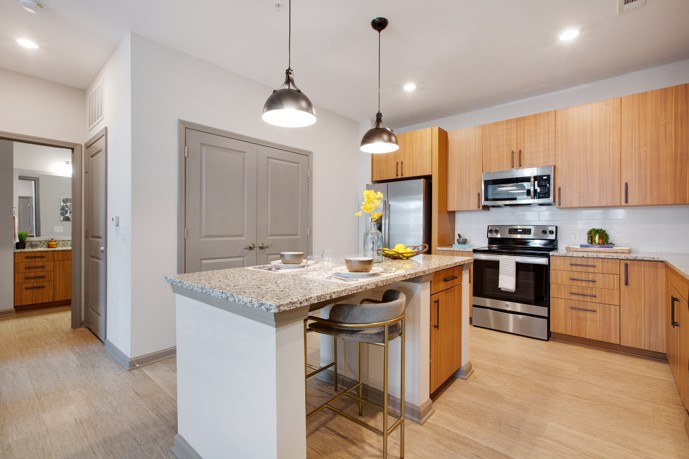At Vesta City Park, you can find a contemporary kitchen equipped with sleek light brown cabinets, a spacious center counter with ample room for a bar stool, and top-of-the-line stainless steel appliances.