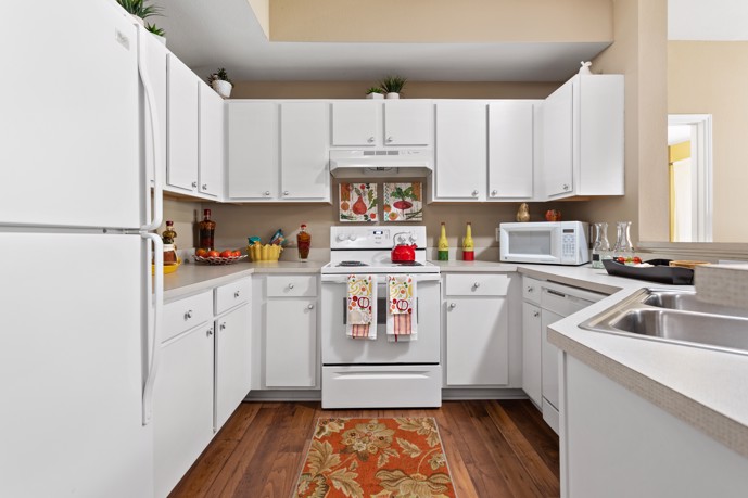 Long view of an apartment kitchen with white cabinets and appliances, grey countertops, and hardwood floors