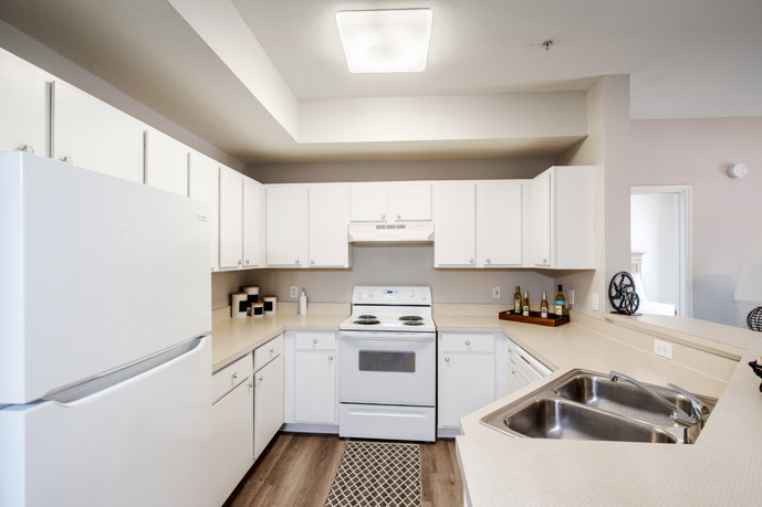 Long view of an apartment kitchen with white cabinets and appliances, grey countertops, and hardwood floors