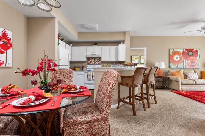 Carpeted beige and red apartment with a view from the dining area that overlooks the kitchen and living area