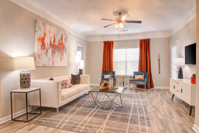 An apartment interior with wood-style flooring, large windows, and white furniture at the Waterford Landing apartments in McDonough, GA.