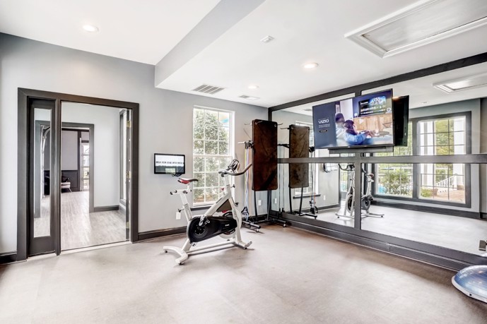 The fitness room at The Village at Auburn, featuring a large mirror, a standing bike, providing residents with a convenient and well-equipped space to stay active and healthy.