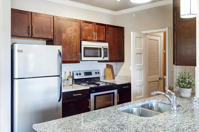 The kitchen within The Shores apartments, featuring rich brown cabinets, sleek white appliances, and luxurious granite countertops, offering a stylish and functional space for cooking and entertaining.