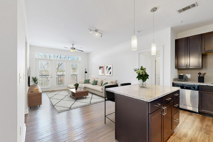 A kitchen with an island  leading to a living room, offering double door access to a balcony.