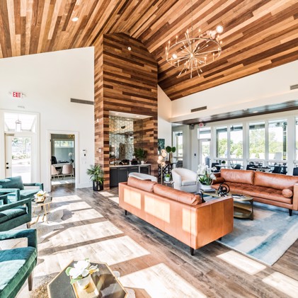 The stylish lounge area at the Virtuoso apartments' clubhouse in Huntsville, AL, featuring a wood-plank ceiling and colorful seating throughout.