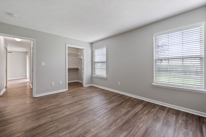 Chic bedroom boasting a walk-in closet, hardwood-style flooring, and abundant natural light from two windows.