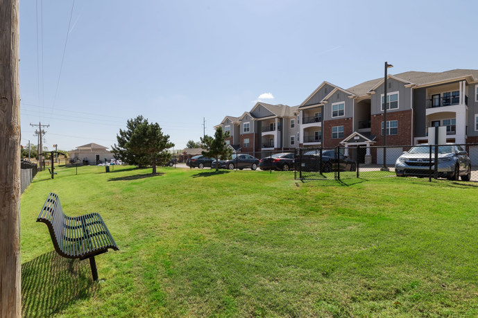 A serene grassy dog park enclosed by a fence and shaded by trees, providing a safe and enjoyable outdoor space for furry companions to roam and play at The Shores.