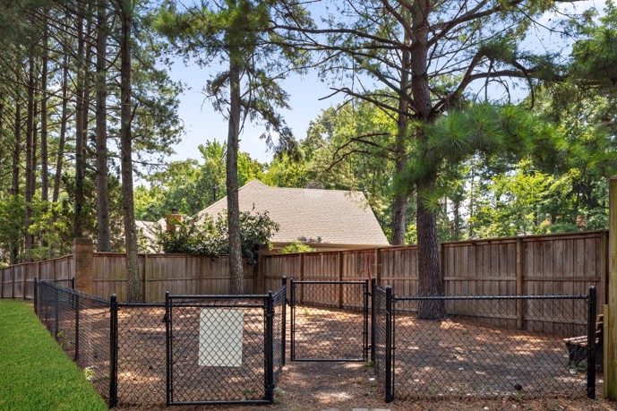 Fenced-in shaded dog park with a wood chip ground surrounded by pine trees 