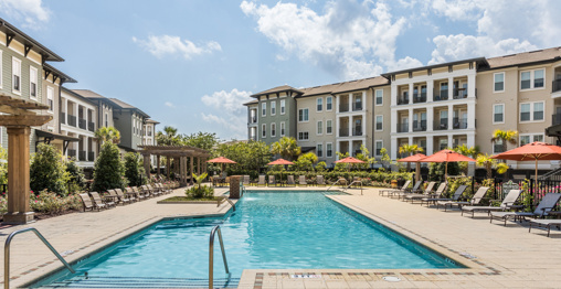 A modern outdoor pool by the clubhouse at a Charleston, SC, apartment with lounge chairs, and umbrellas for residents comfort.