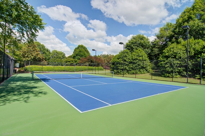 A serene fenced tennis court nestled among lush trees, offering a tranquil space for recreation at Waterford Landing in McDonough, Georgia.