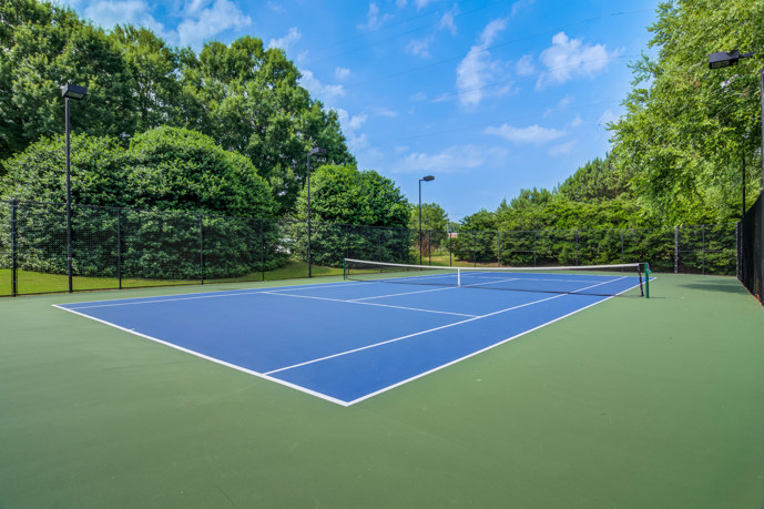A serene fenced tennis court nestled among lush trees, offering a tranquil space for recreation at Waterford Landing in McDonough, Georgia.