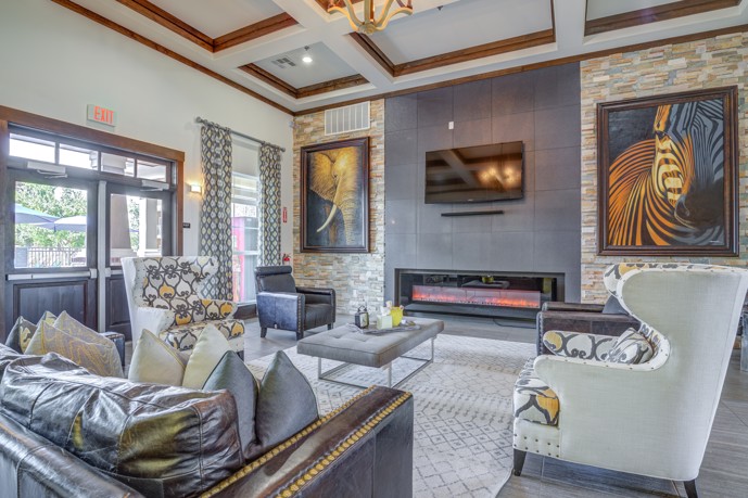 The elegant clubhouse lounge at The Shores apartments, exuding sophistication with a welcoming fireplace, expansive windows providing panoramic views, and luxurious leather seating, offering residents a refined space for relaxation and socializing.