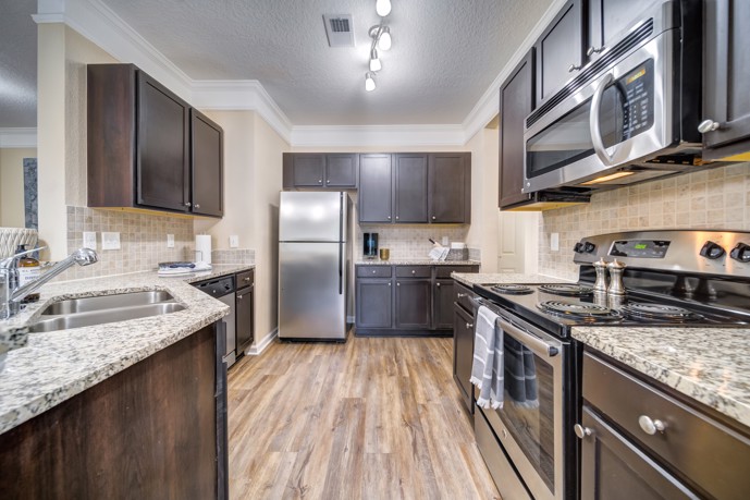 A spacious kitchen boasting dark wood cabinets, sleek quartz countertops, and modern stainless steel appliances, providing a stylish and functional culinary space within Waterstone at Brier Creek.