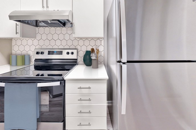 A sleek and modern kitchen boasting quartz countertops, a pristine white tiled backsplash, and gleaming stainless steel appliances, offering residents a stylish and functional culinary space at The Residences on McGinnis Ferry apartments in Suwanee, GA.