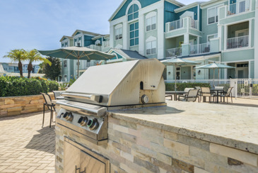 Outdoor grill area with grilling stations, picnic tables, and surrounded by greenery at The Enclave at Tranquility Lake.
