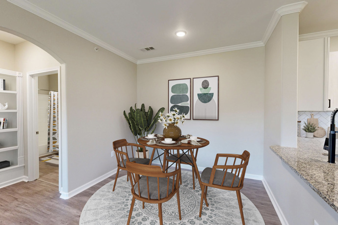 A dining room adorned with a table for shared meals and gatherings, with a hallway leading to the private bedrooms within The Shores apartments.