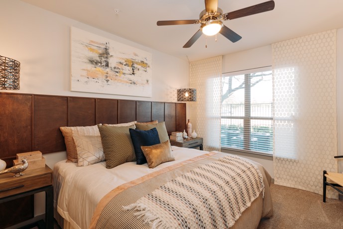 Comfortable bedroom featuring a window for natural light, plush carpet flooring, and a cooling ceiling fan.