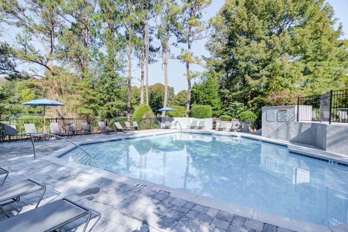 The pool at the 1800 at Barrett Lakes is surrounded by lush greenery and families enjoying a sunny day.
