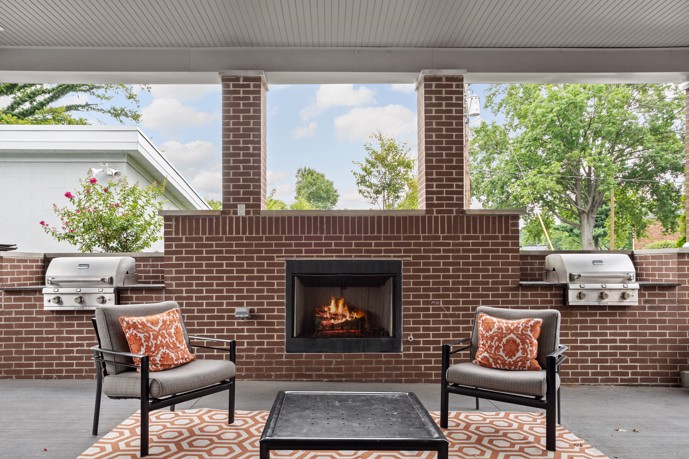 Outdoor community lounge, sheltered and adorned with a fireplace, two barbecue grills, and comfortable seating arrangements.