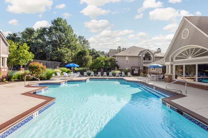 Outdoor swimming pool with trees and deck chairs along the far end of apartments in Louisville, KY