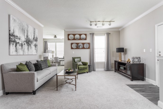 A cozy living room featuring a comfortable two-seater couch, a separate work area, and a carpeted floor, at The Village at Auburn in Durham, NC. 