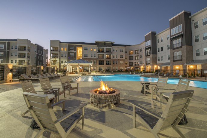 Outdoor community firepit with chairs around it in a circle and a swimming pool and the apartment buildings behind it and to the right