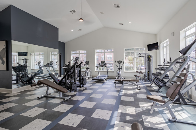 A well-equipped gym featuring cardio and weight equipment, large windows for natural light, and ceiling fans for comfort.