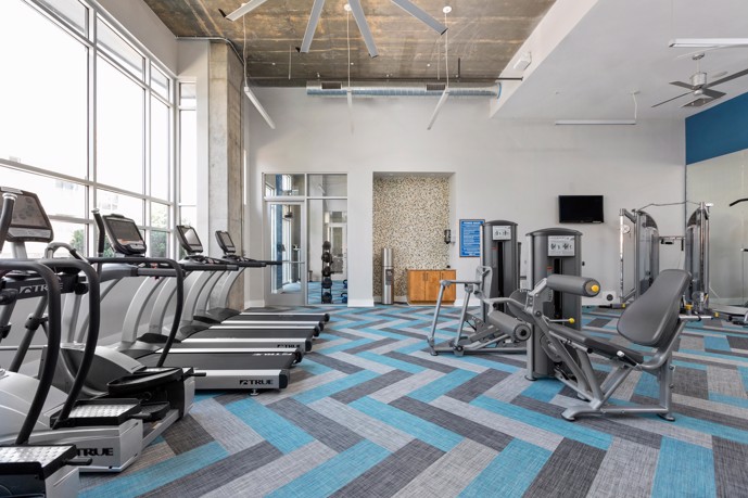 Fountains Southend's gym, surrounded by floor-to-ceiling windows, top-notch exercise equipment, and refreshing ceiling fans.