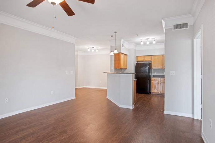 Long view of an empty apartment at Carrington Park at Huffmeister with hardwood floors, grey walls, a ceiling fan, and an open kitchen in the background