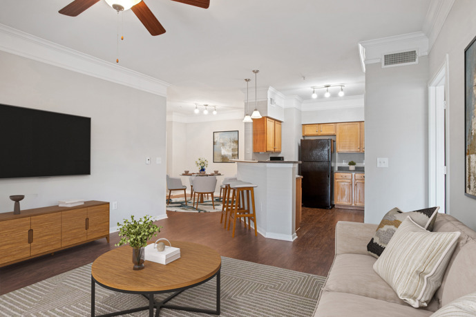 Long view of an empty apartment at Carrington Park at Huffmeister with hardwood floors, grey walls, a ceiling fan, and an open kitchen in the background
