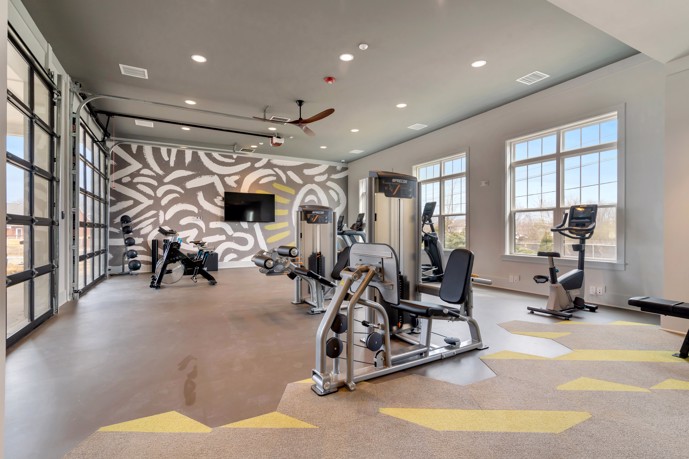 Fitness center featuring modern garage-style doors, ample windows, and a variety of exercise equipment.