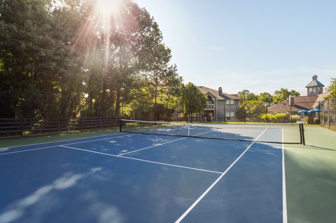 Outdoor blue tennis court with sun shining down on it through the trees