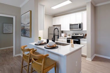 At The Pointe at Vista Ridge, you'll find a kitchen equipped with stainless steel appliances, white cabinets, and a bar counter with two stools, offering a modern and functional space for cooking and dining.