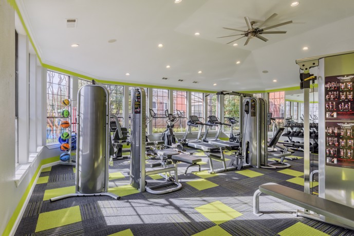 A colorful fitness center at The Delano at North Richland Hills with gym equipment, large windows, and carpeting at North Richland Hills, TX. 