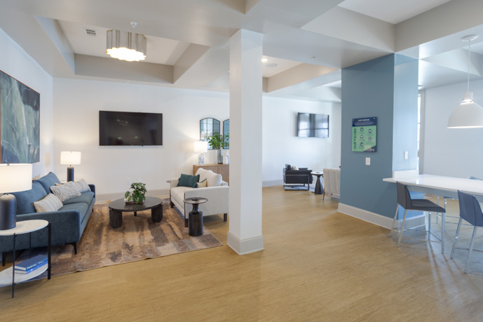 Apartment community clubhouse  with two seating areas and a dining table between two pillars that are under pendant lighting