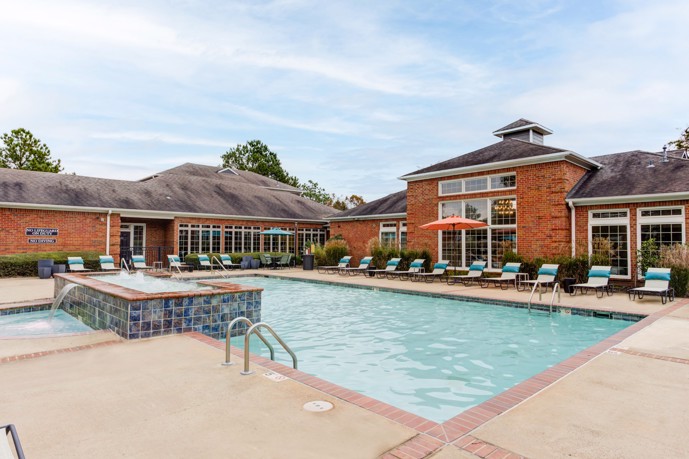 A sprawling brick clubhouse adorned with a stunning resort-style pool, complete with comfortable loungers, at Walnut Hill apartments in Memphis, Tennessee.