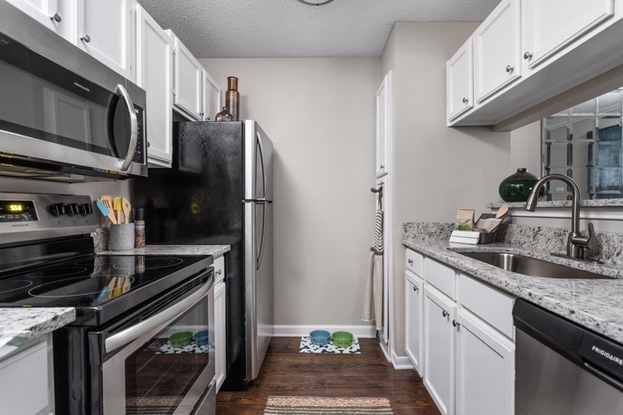 Narrow apartment kitchen with white cabinets, grey granite countertops and walls, and stainless steel appliances