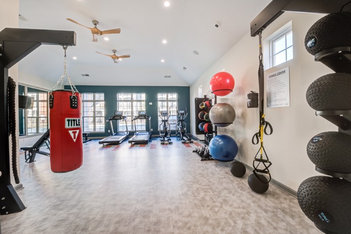Long view of a community fitness center facing windows with exercise balls, equipment, and a large punching bag