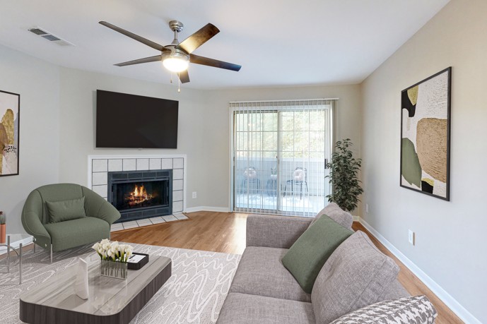 Relax in the comfortable living room at The Landings of Brentwood, complete with a cozy fireplace, wall-mounted TV, and a stylish green couch.