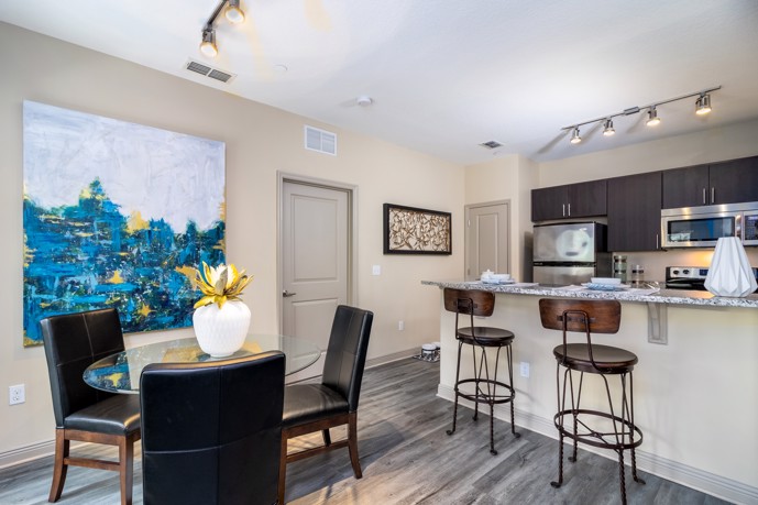 Welcoming dining area seamlessly integrated with an open kitchen, complete with a breakfast bar, stylish track lighting, sleek stainless steel appliances, and durable wood-style flooring.