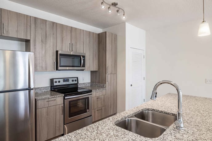 Welcoming open kitchen, complete with a breakfast bar, stylish track lighting, sleek stainless steel appliances, and durable wood-style flooring.