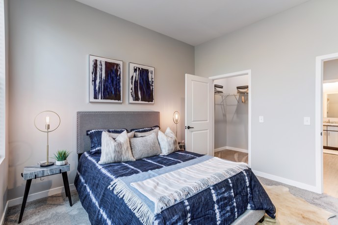 An inviting bedroom within a Views of Music City apartment, adorned with a queen bed dressed in soothing blue linens, flanked by two side tables, and featuring a spacious closet for storage.