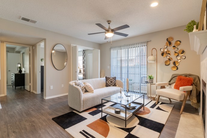 A modern and spacious living room within The Augusta apartments, featuring elegant wood-style flooring, sliding doors opening onto a balcony, and a hallway leading to the bedrooms, offering a comfortable and inviting living space.
